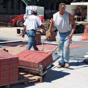 2 construction workers using a pave cart to move pavers from the truck to the worksite